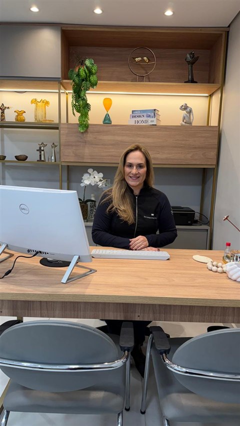 Dra. Luciane sentada à mesa, vista a partir das cadeiras do consultório